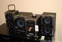 Full system including main unit, subwoofer, and two speakers shown on table.
