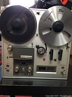 Front-facing view showing two reels on aluminum panel, control knobs, VU meters.