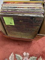 Photo of vinyl records in a box with Alice Cooper's 'School's Out' album visible on top, including a green sticker with album notes and pricing.