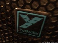 Close-up of Yorkville logo on speaker grille, showing front protective metal grille and logo badge.