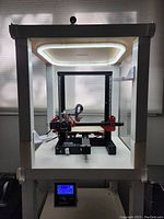 Frontal view of printer inside white enclosure with overhead LED light and control console visible