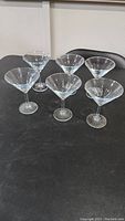 Side view of six clear glass martini glasses arranged in two rows on a black surface, showing conical bowls and slender stems.