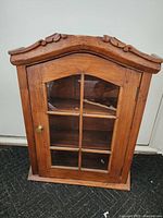 Front view of antique wooden wall cabinet with glass paneled door and carved top