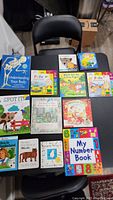 Photo of all 11 children's books displayed on a black table with a black chair in the background.