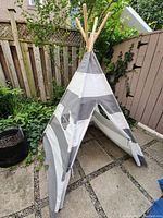 Full view of the children's canvas indoor play teepee outside on stone patio showing front with open doorway and natural wooden poles