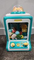 Front view of claw machine toy showing control panel, stuffed plush toys inside, and cat figure on top dome.