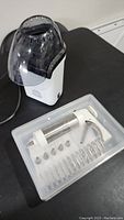Photo shows white electric popcorn maker with black chute and lid, and transparent cookie press set with multiple metal nozzles and discs in plastic case.