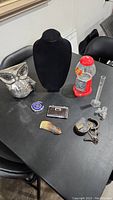 Full lot of items on black table surface showing chrome owl, necklace bust, Jelly Belly dispenser, compact, horn hair comb, opera glasses, and lab vials.