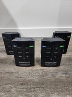 Four black Monster Powernet 200 Ethernet powerline adapters standing upright on a wooden floor. Each unit has a front-facing pass-through electrical outlet and LED indicator lights.