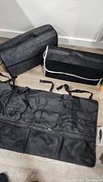 Two felt car trunk organizer bags and one large black cargo net laid on the floor showing their size and layout.