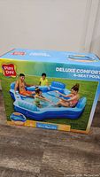 Photo of sealed boxed inflatable pool with adult and children model showing the pool in use on grass background