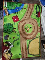 View of the full farm-themed playmat showing paths, farm buildings, trees, a pond, a picnic area, a fenced sandbox or pasture area, and playground equipment.