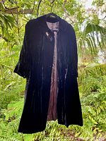 Front view of black velvet vintage theater coat hanging among greenery, showing full length and sleeve details