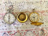 Photo showing the Gallet stopwatch, the inside of the gold tone pocket watch case back, and the face of the Andre Rivalle pocket watch with Roman numerals and subdial.