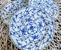 Four Royal Tettau porcelain plates with blue floral and vine design and scalloped edges, shown stacked and individually on a white woven surface.