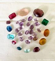 Wide view of most of the 33 loose stones showcasing variety of colors and shapes including purples, blues, greens, reds, pinks, and browns.