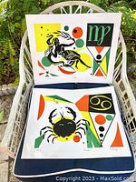 Full view of two signed and numbered vintage serigraphs displaying Virgo and Cancer astrological designs on a white chair outdoors.