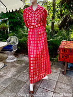 Front view of the red geometric pattern maxi dress displayed on a mannequin outdoors, showing the full length and flow of the skirt with the matching belt.