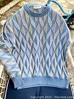 Full front view of the pullover sweater showing geometric blue and gray pattern and ribbed neckline, cuffs, and hem.
