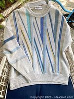 Full view of light grey vintage 80s Norm Thompson pullover sweater with vertical stripe design in blue, teal, and yellow on mesh chair outdoors