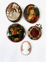 Group photo showing all five items including brown cameo brooch, painted portrait pin, Russian lacquer pin, white cameo, and child's cameo ring.