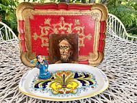 Photo displaying the red and gold Florentine serving tray with ornate gilt design, the miniature oil painting portrait on tin, the Italian ceramic platter, and the blue clay angel figurine.