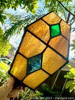 Close up held photo showing amber textured glass panels with green and blue diamond shaped colored glass pieces, sunlight behind shows translucency.