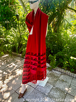 Mannequin wearing the large red alpaca wool scarf with black embroidery along one edge, draped long to show full length and fringes.