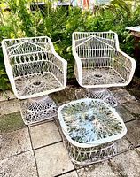Full set showing two chairs and matching glass top table outdoors on paving with greenery