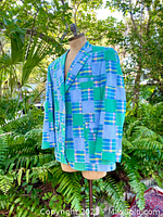Side angle view of vintage 1980s Madras patchwork blazer featuring blue and green plaid square patterns on a dress form outside with foliage in the background.