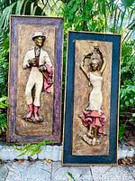 Front view showing both figurative fiberglass sculptures framed in rectangular frames, positioned side by side outdoors surrounded by greenery.