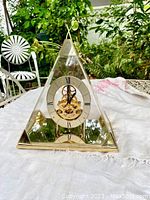 Front view of vintage Seiko skeleton clock with pyramid clear dome and metal base on white fabric outdoors.