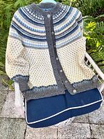 Vintage handmade Norwegian hand knit cardigan sweater with pewter buttons displayed on chair outdoors, showing overall condition including discoloration on bottom right front.