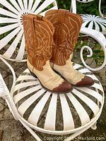 Pair of vintage two-tone leather cowgirl boots placed on a white metal chair, showing front angle with brown stitched upper shaft and beige bottom half.