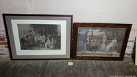 Two framed art prints leaning against a wall on a wooden floor. Left print is black and white engraving titled 'Two's Company'. Right print is colored engraving titled 'The Drummond Family' by Lawrence Josset.