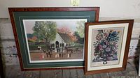 Two framed prints leaning against a wall; larger one is wedding lithograph, smaller is floral print.