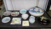 Full lot showing a variety of artisan pottery and ceramics including plates, bowls, and a covered dish.