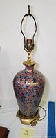 Full view of the tall enameled brass lamp showing the floral pattern on the bulbous body, brass neck, and fitting parts.