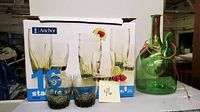 Photo shows the boxed Anchor Hocking 16-piece Starfire glass set with two short glasses and a green glass wine chilling bottle with stopper and string next to the box.