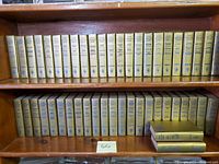 Full view of two wooden bookshelf sections filled with 66 Golden Harlequin Library hardcover romance novels with gold textured covers and blue embossed text on spines.