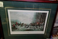 Framed engraving print showing a fox hunting scene with riders and dogs in a natural landscape, clear view of artwork and frame.