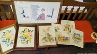 Framed Irish Prayer watercolor alongside some framed and unframed theorem paintings featuring flowers and fruits placed on an orange bench
