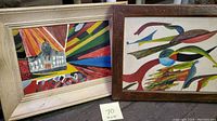Two framed abstract oil paintings on canvas side by side on a wooden surface, one with a beige frame and the other with a dark carved wooden frame, sizes approximately 19x15 inches each