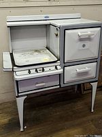 Front view of the vintage White Star Heet Master stove showing tray, control knobs, drawer, and oven doors.