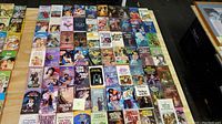 Top-down view of approximately 52 vintage romance pulp fiction paperback books laid out side by side in rows, showing full covers. Covers colorfully illustrated with romantic themes, typical of 1960s and 1970s romance novels.