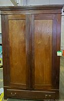 Front view of vintage wooden armoire cabinet with two paneled doors and bottom drawer with metal handles.
