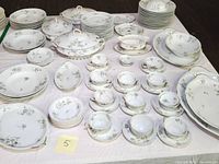 Wide view of china set laid on table showing major pieces including plates, bowls, cups, saucers, covered serving dish, serving platters.