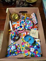 Box of various vintage metal party noise makers with colorful painted designs and plastic handles