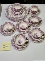 Full view of the purple transferware set including multiple teacups on saucers and stacked dinner plates showing the detailed pastoral scenes.