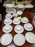 Full view of the set on a wooden surface, showing multiple teacups, saucers, bowls, and plates arranged